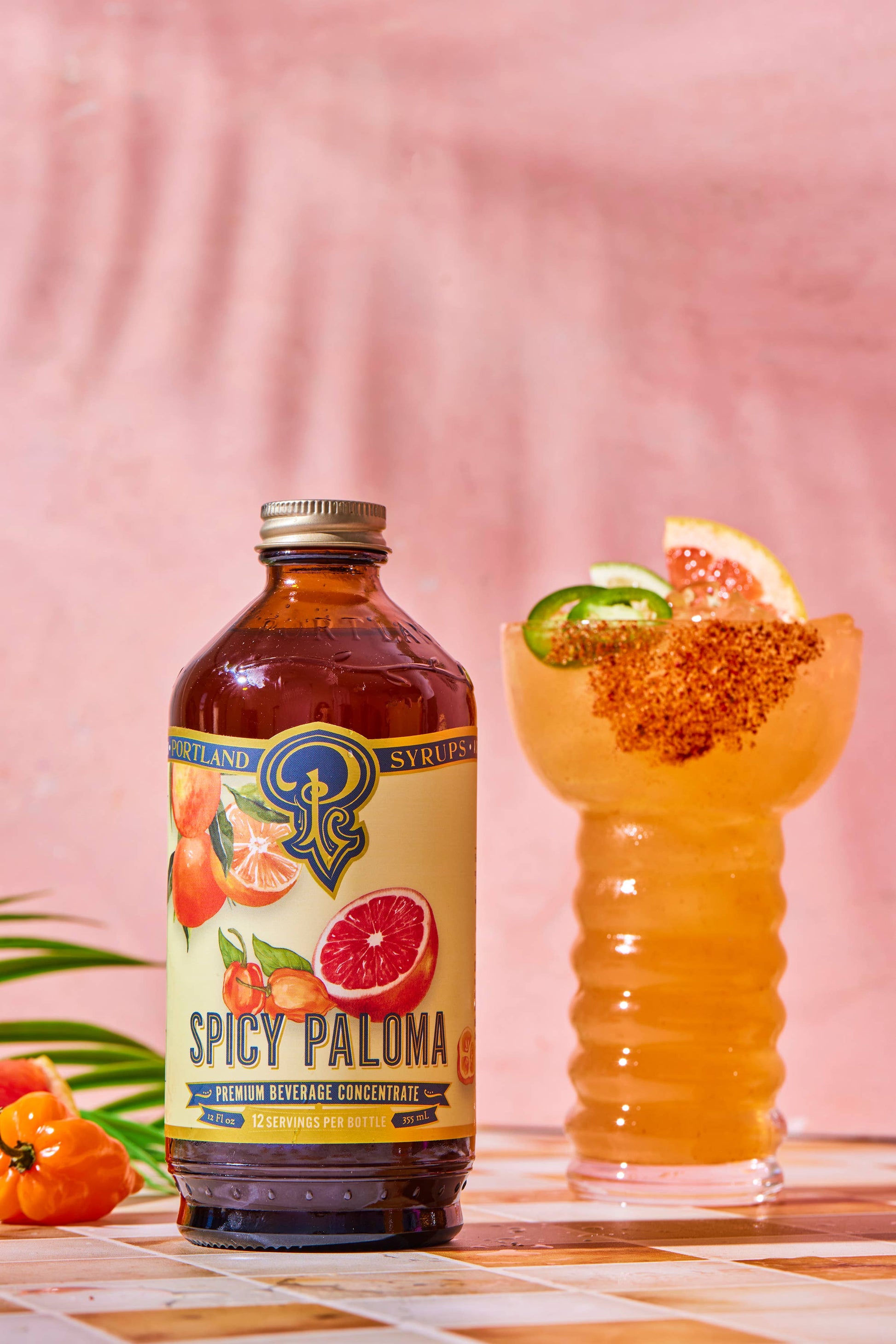 Spicy Paluma syrup bottle with a cocktail in the background on a checkered tablecloth.