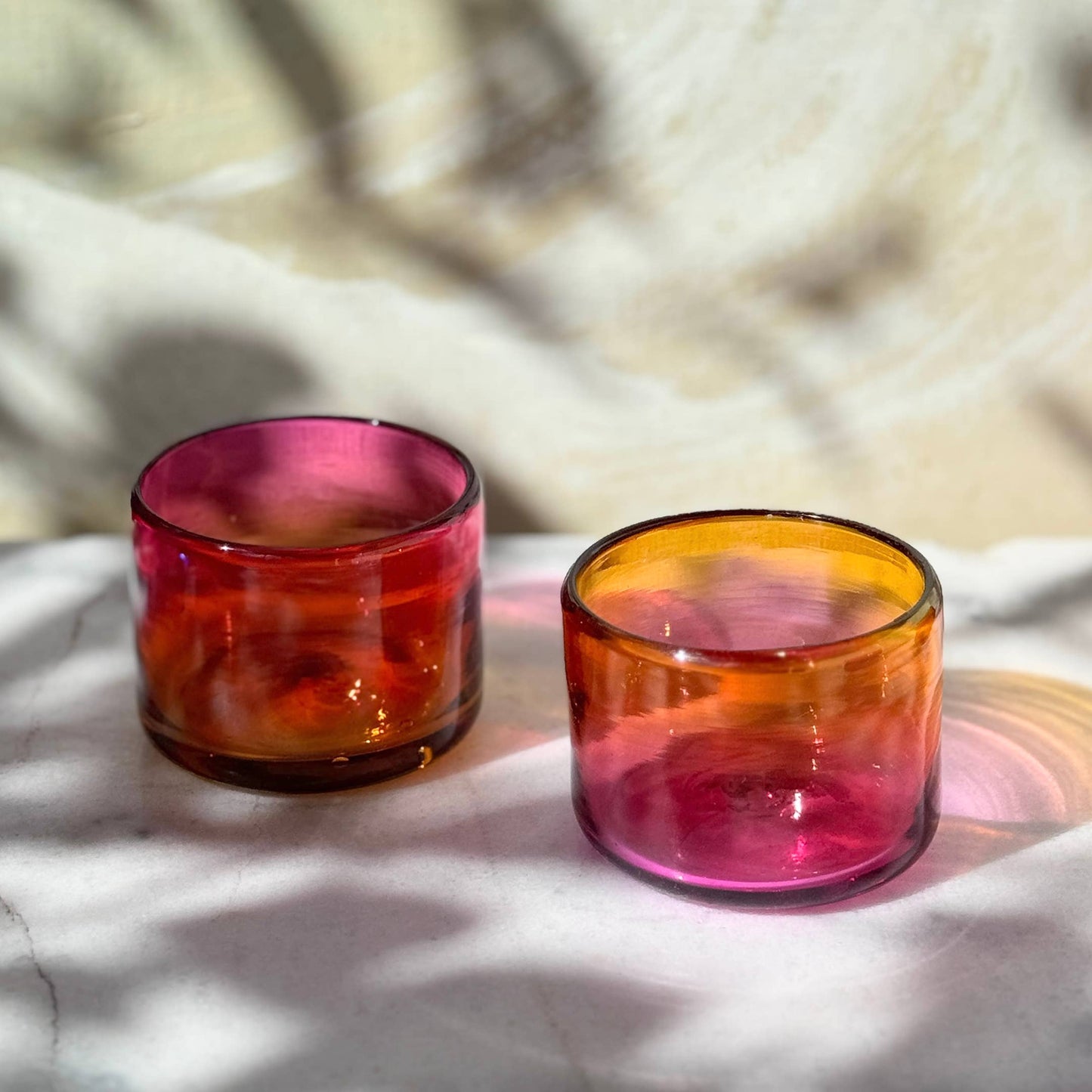 Two colorful glasses on a textured surface with a blurred natural background.