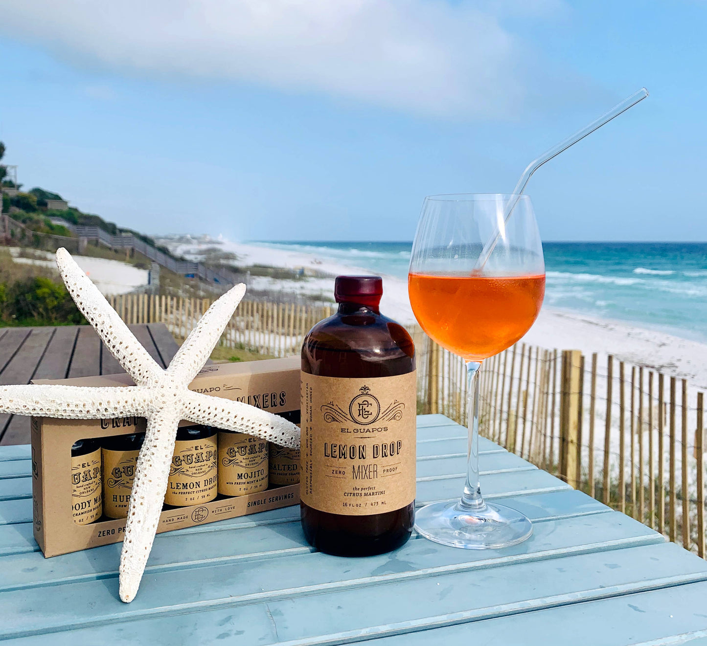 Bottle of lemon drop mixer with a glass of cocktail on a beach setting