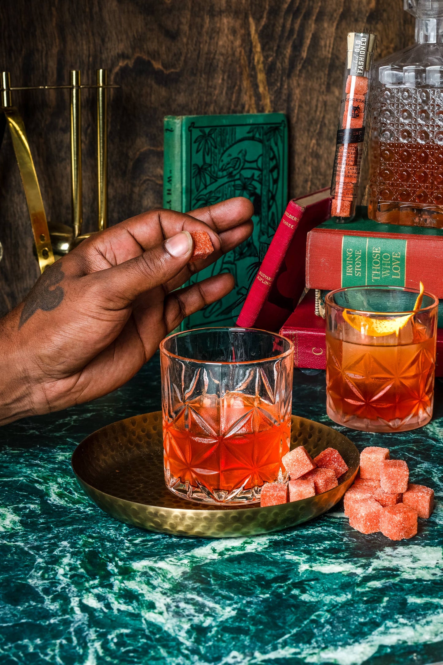 Cocktail with ice cubes on a green marble surface, with a hand holding a small book.