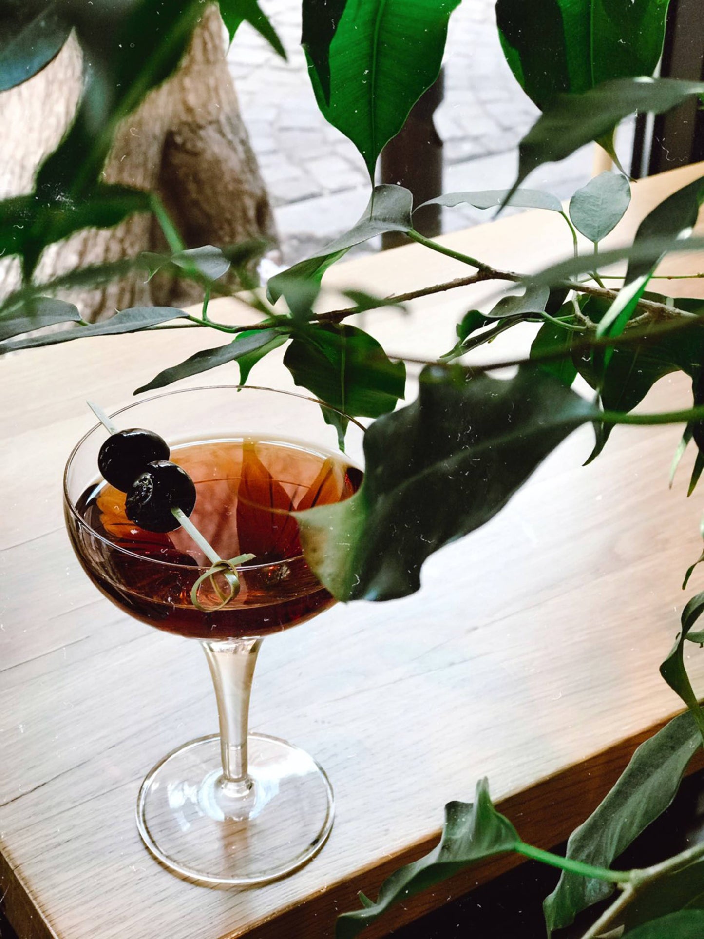 Cocktail with cherries in a glass on a wooden surface with green leaves in the foreground