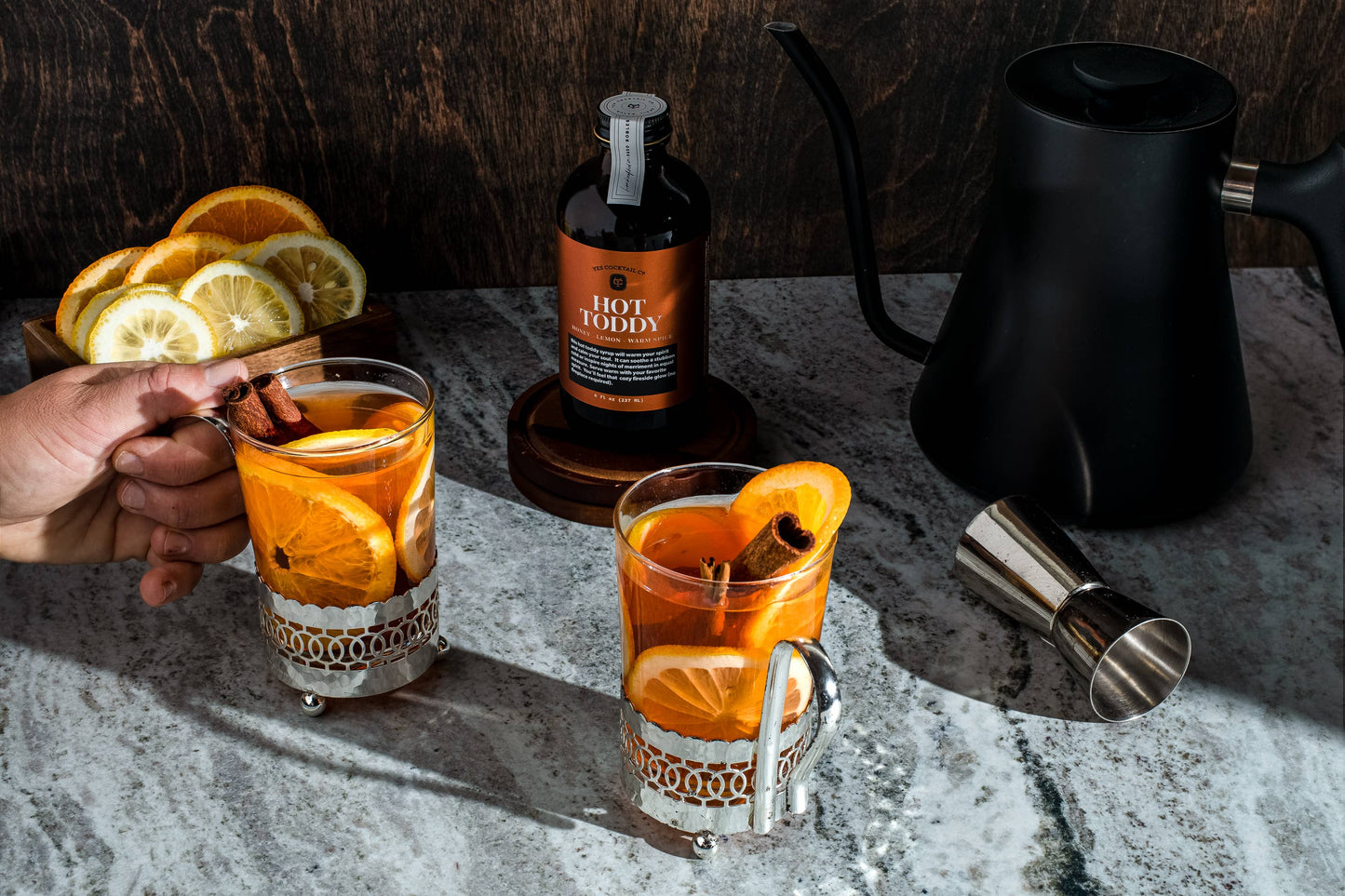 Two glasses of orange cocktail with a bottle and kettle on a textured surface