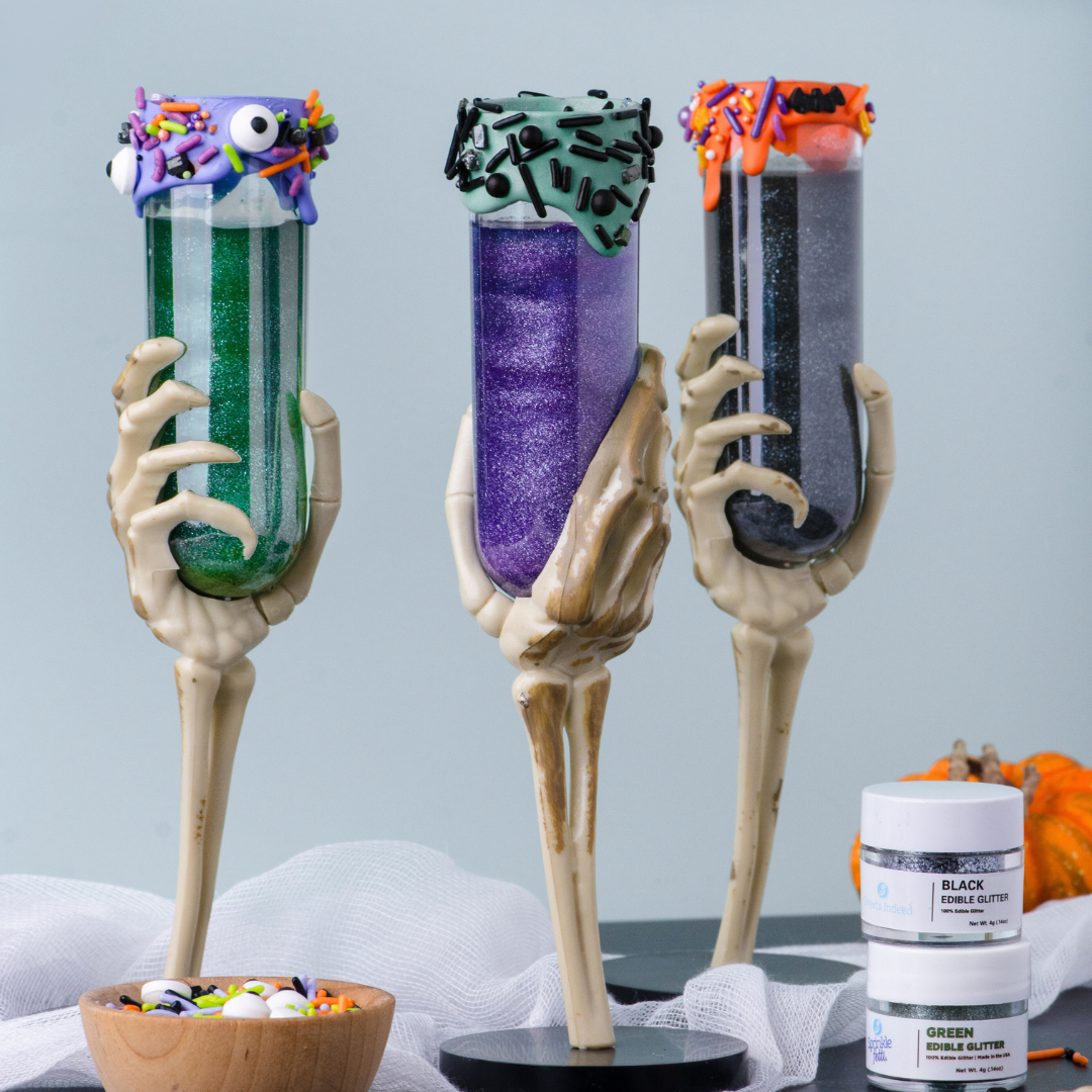 Halloween-themed sparkly cocktails in skeleton hand glasses against a light blue background.