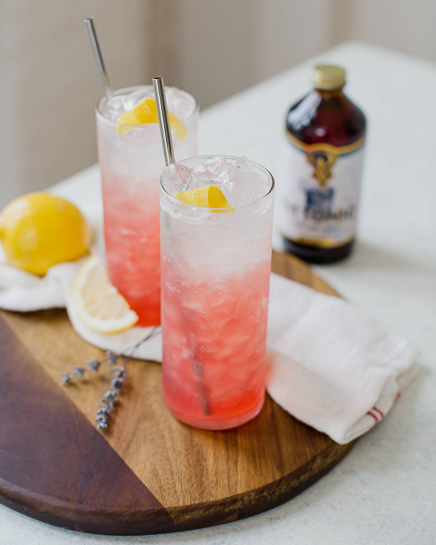 Two pink cocktails with lemon slices on a wooden board, accompanied by a bottle of Absolut Vodka.