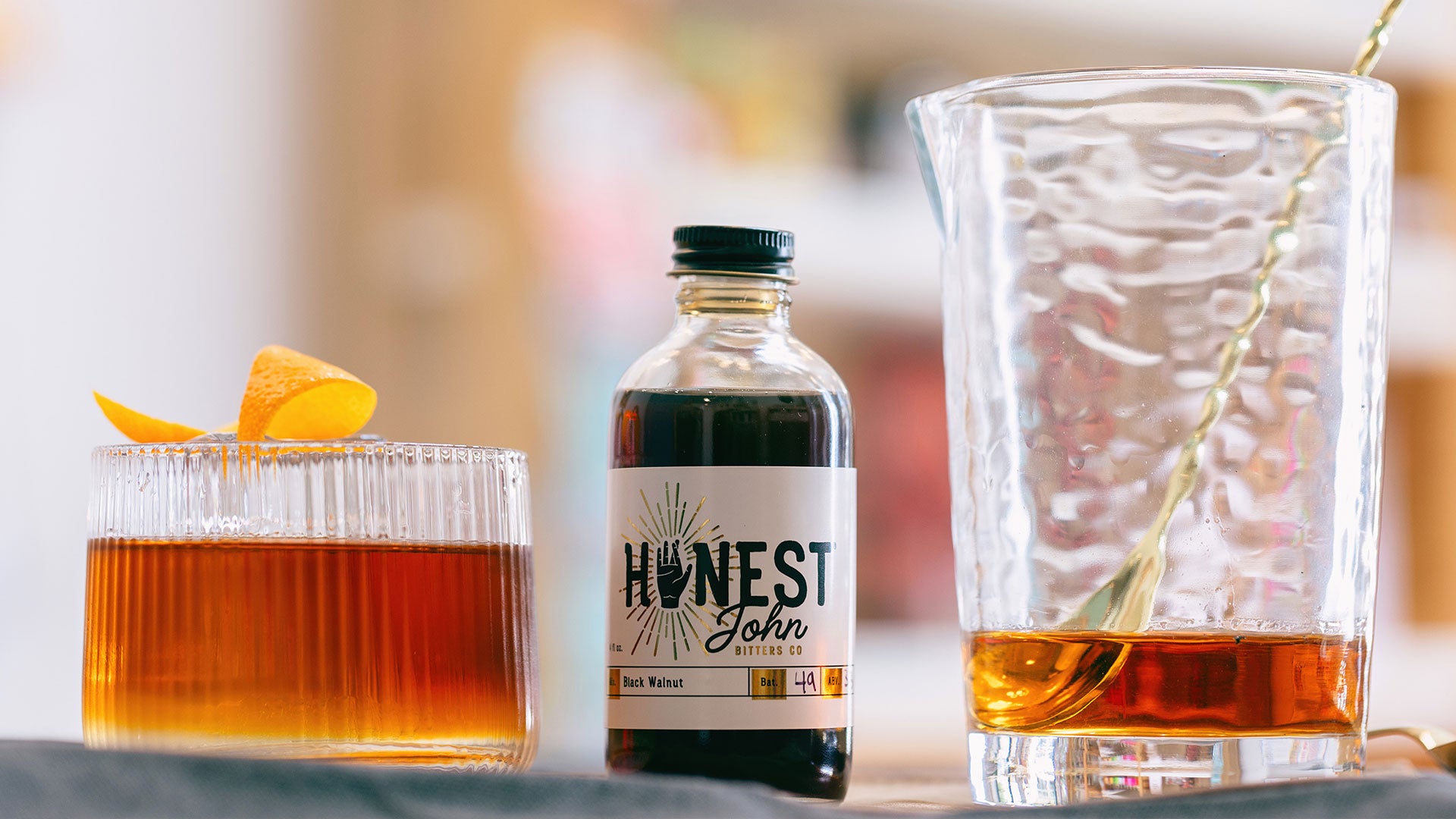 Beautiful glass with alcohol and garnish, bottle of Bitters, and stirring glass with stirring spoon.