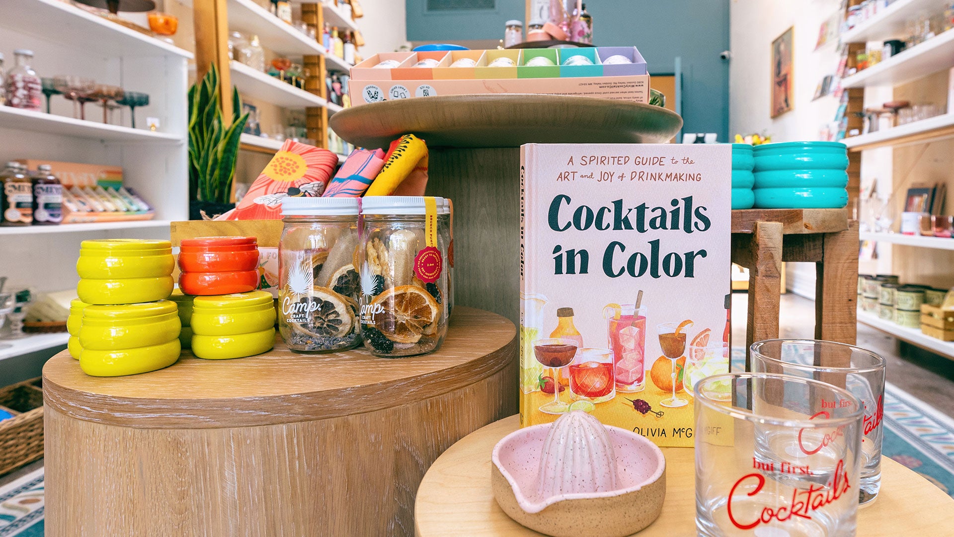 Candles, tea towels, cocktail infusion kits, cocktail book, glasses, and juicer on tables in our retail shop.