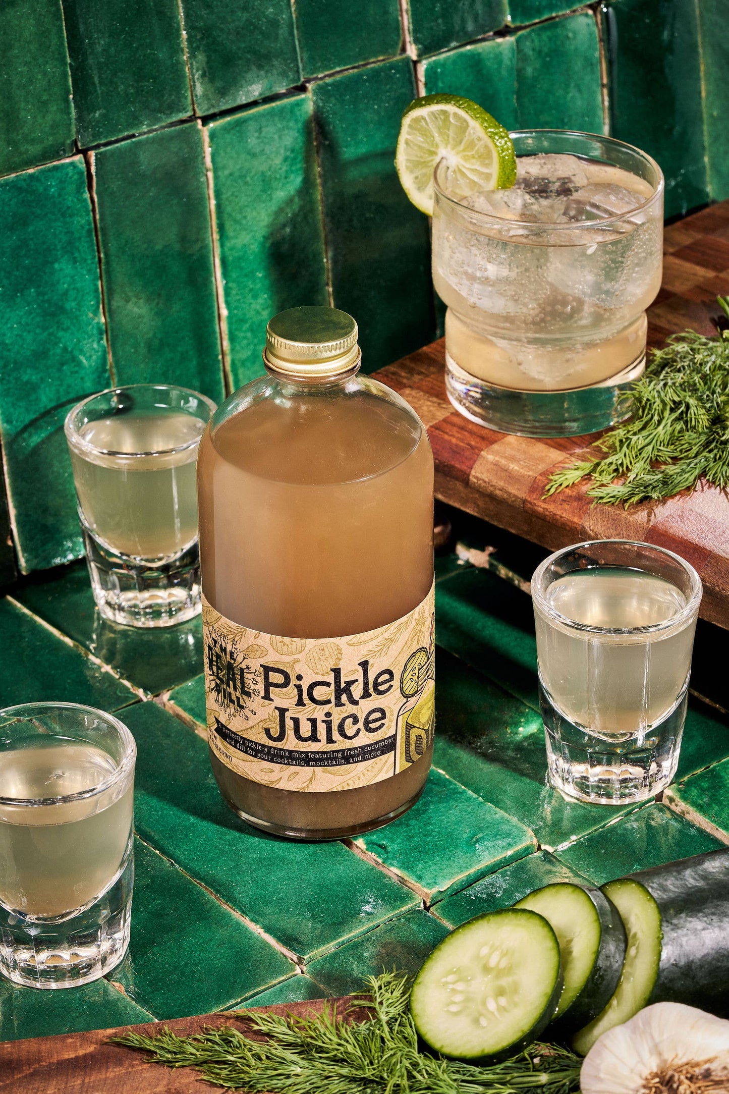 Pickle Juice bottle with glasses of liquid on a green tiled surface