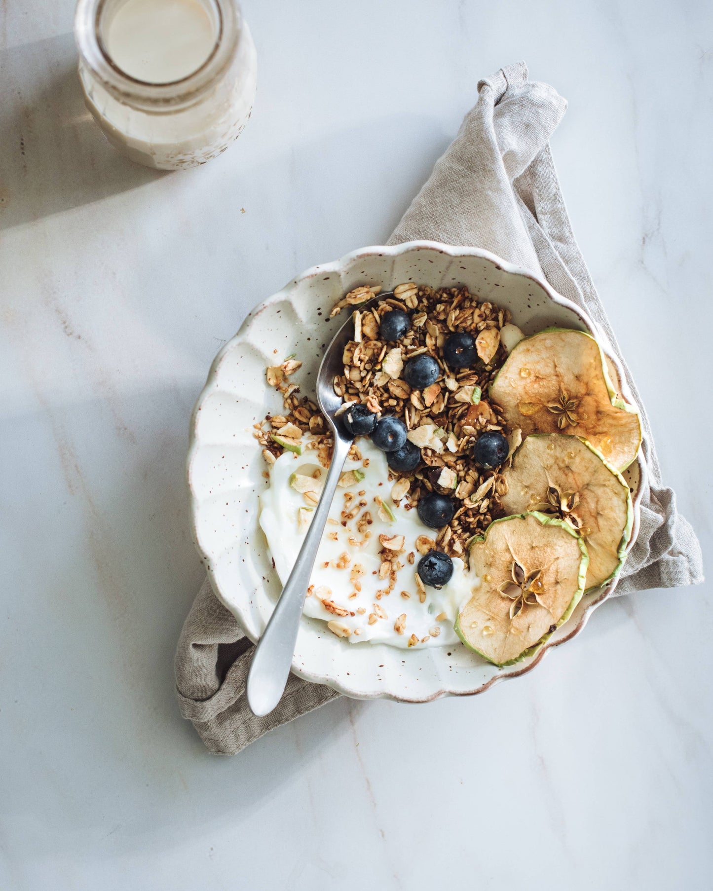 Yogurt bowl with granola, apples, and blueberries on a marble surface