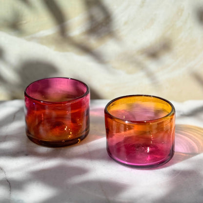 Two colorful glasses on a textured surface with a blurred natural background.