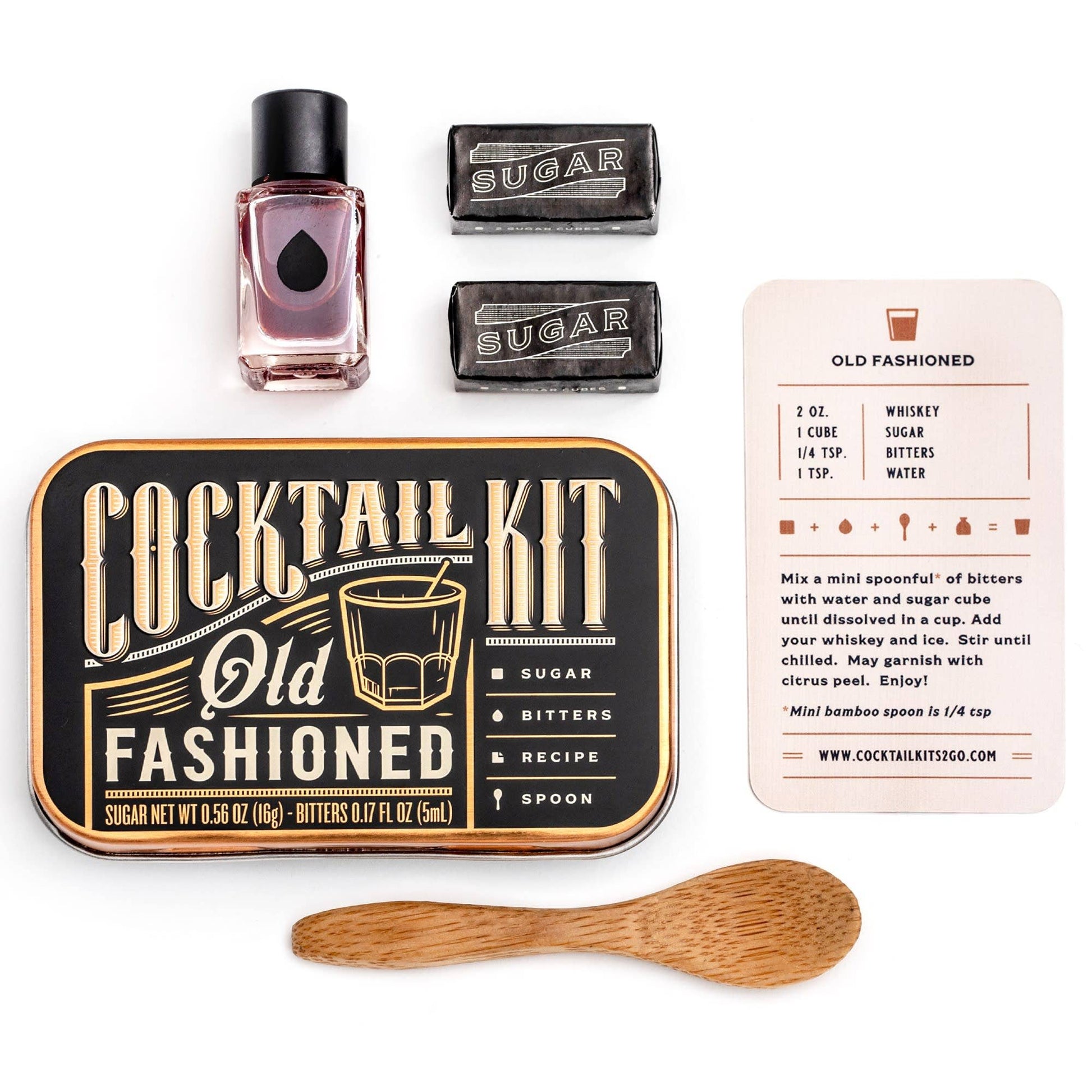 Cocktail kit with Old Fashioned recipe card, bottle, sugar cubes, and wooden spoon on a white background