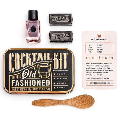 Cocktail kit with Old Fashioned recipe card, bottle, sugar cubes, and wooden spoon on a white background