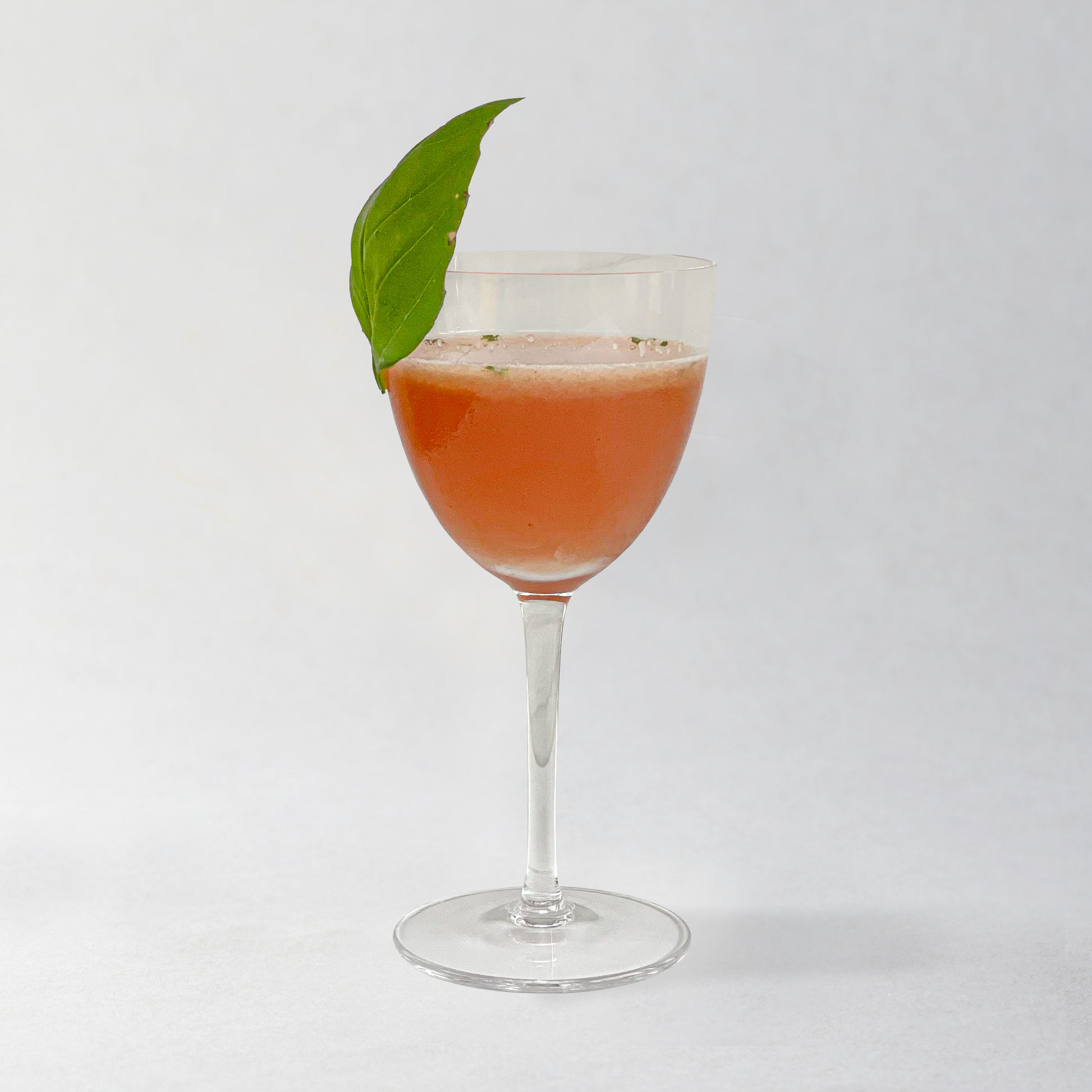 Cocktail in a glass with a green leaf garnish on a white background