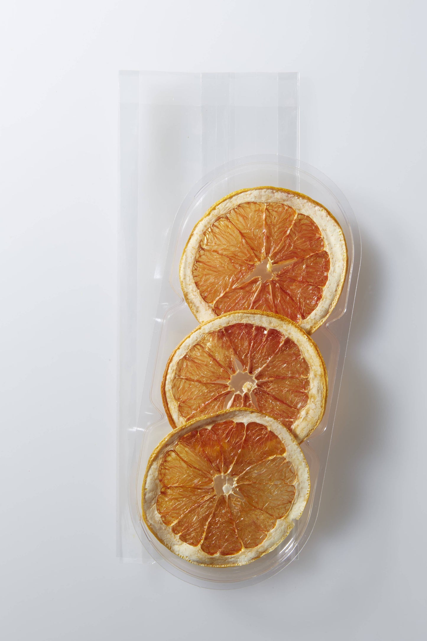 Three dried orange slices in a clear plastic packaging on a white background