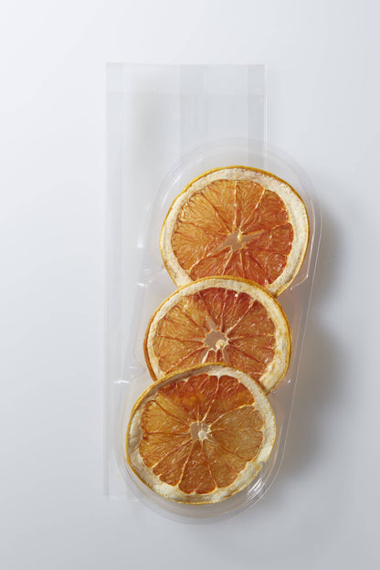 Three dried orange slices in a clear plastic packaging on a white background