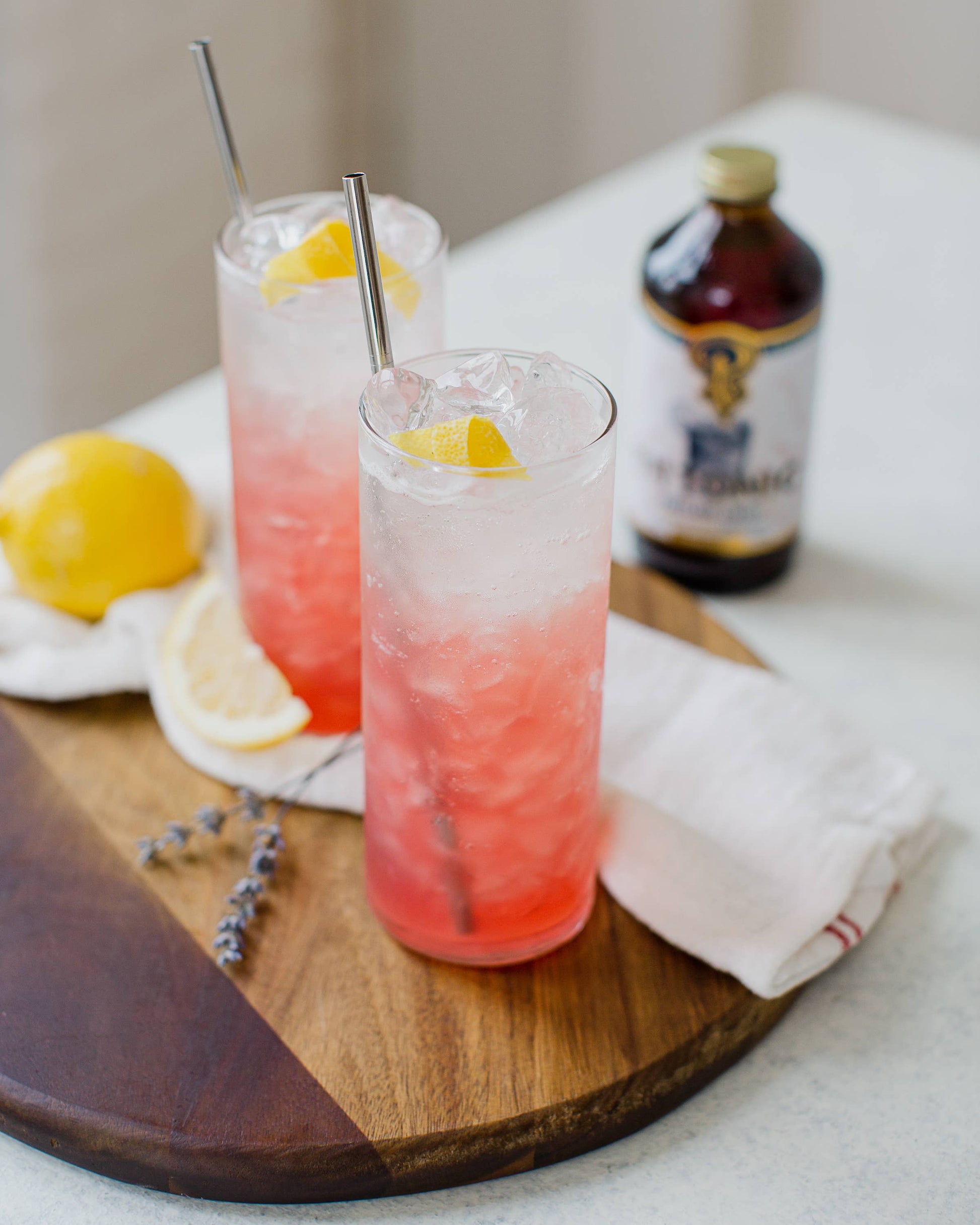 Two pink cocktails with lemon slices on a wooden board, accompanied by a bottle of Absolut Vodka.