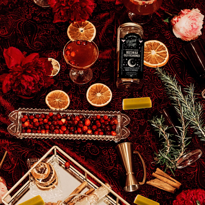 Bottle of Beeswax Old Fashioned Infusion Kit with whiskey, garnishes, and a glass on a dark surface.