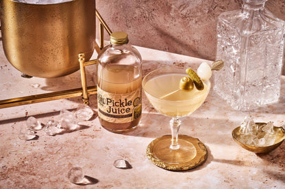 Bottle of 'Pickle Juice' with a cocktail garnished with a pickle on a bar counter.